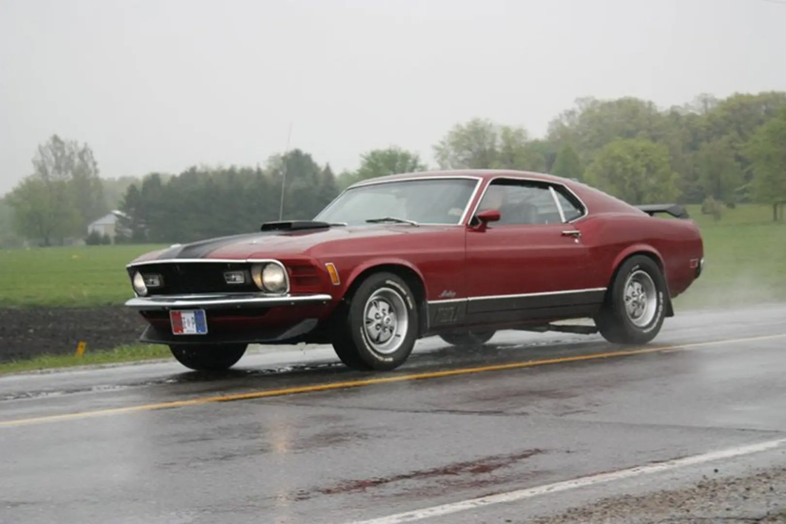 Classic red muscle car driving on wet road.
