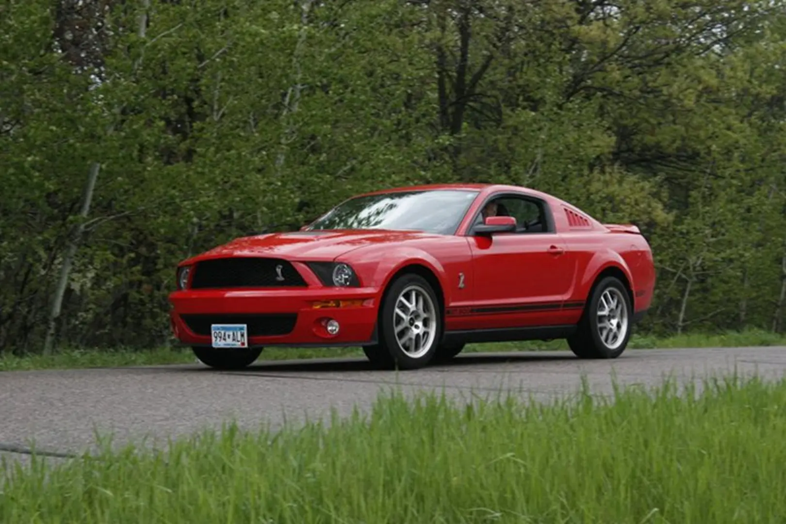 Red Mustang parked by green trees