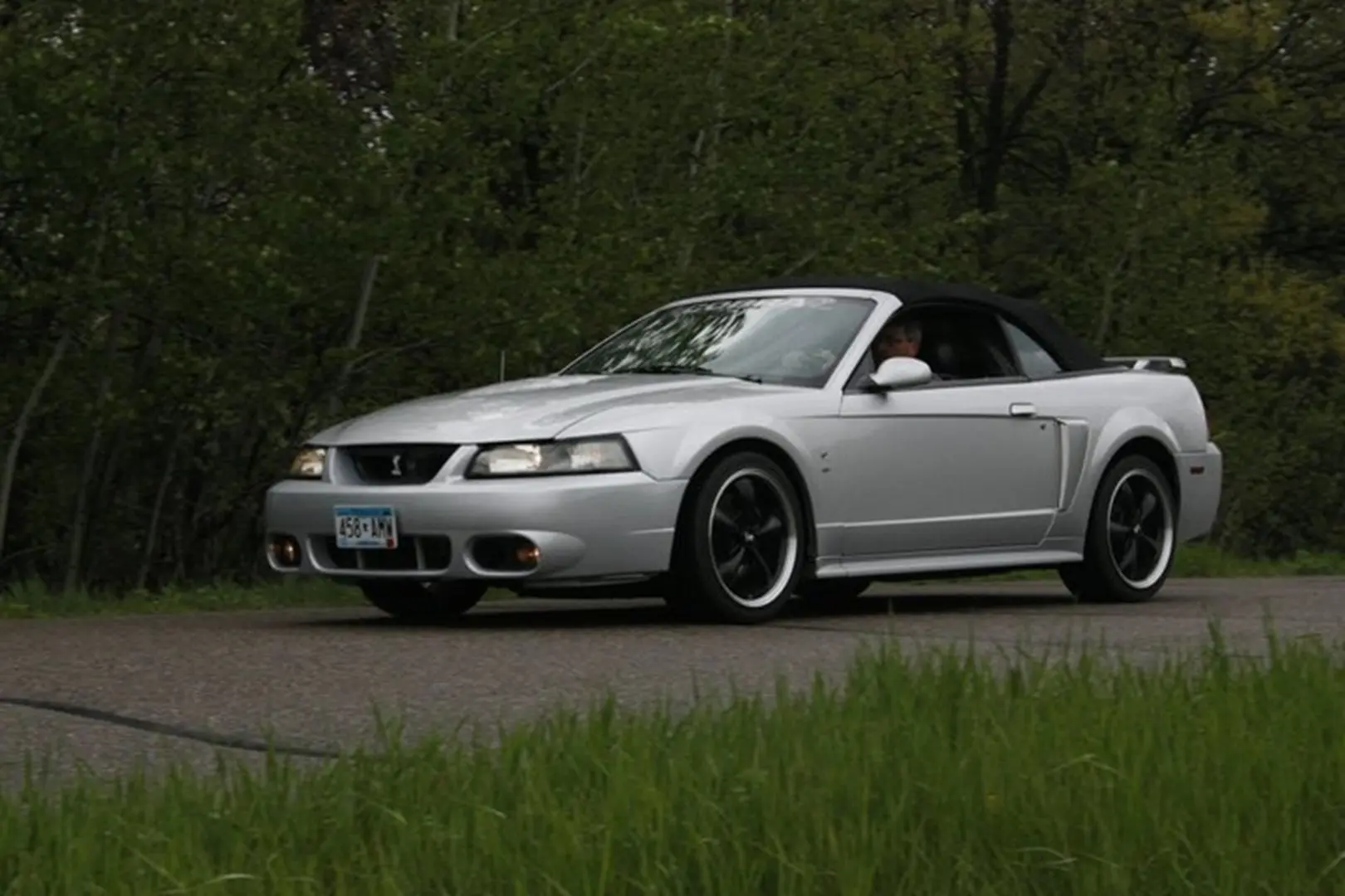 Silver convertible driving on a forest road.