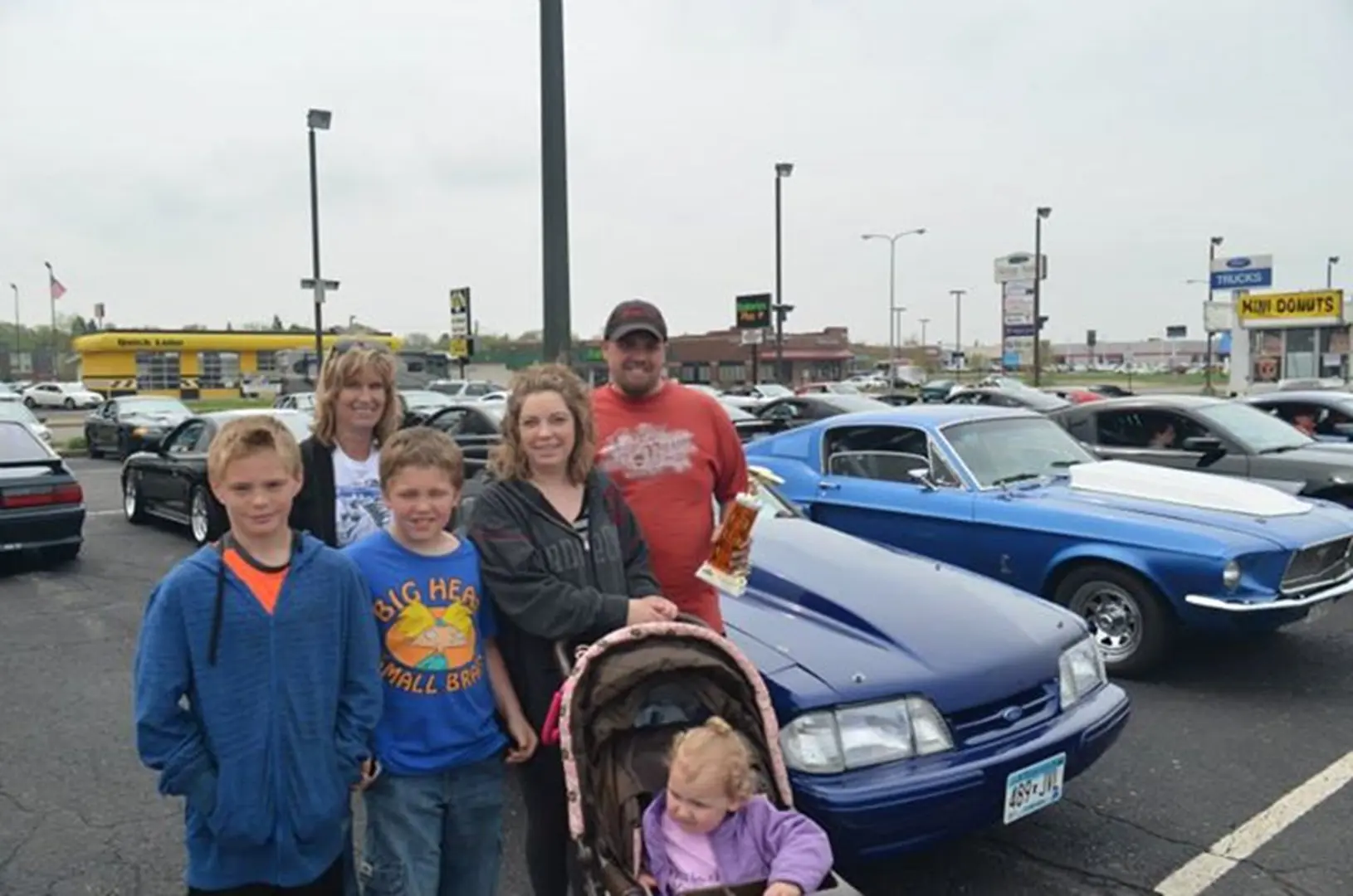 Family posing by classic cars in parking lot