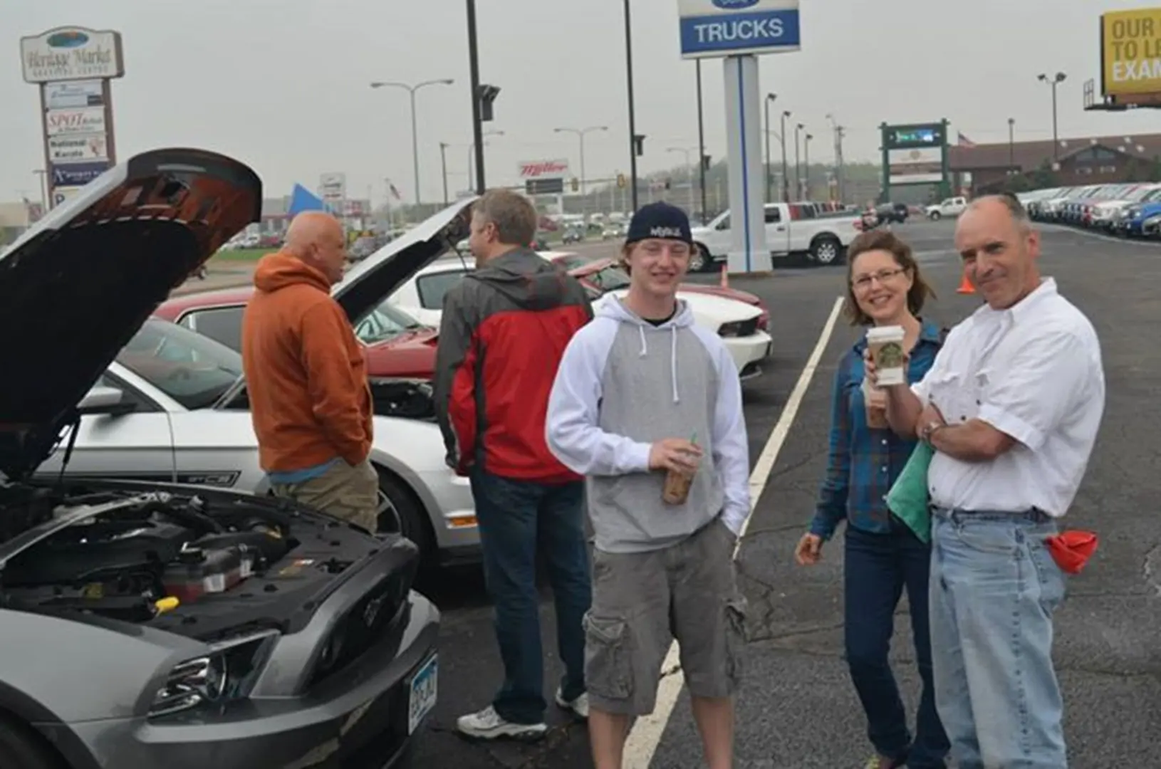 Friends with drinks in car dealership lot